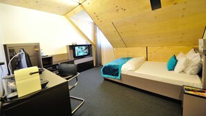 Une chambre d’hôtel avec un lit, un bureau, une chaise, une télévision et un plafond en bois.