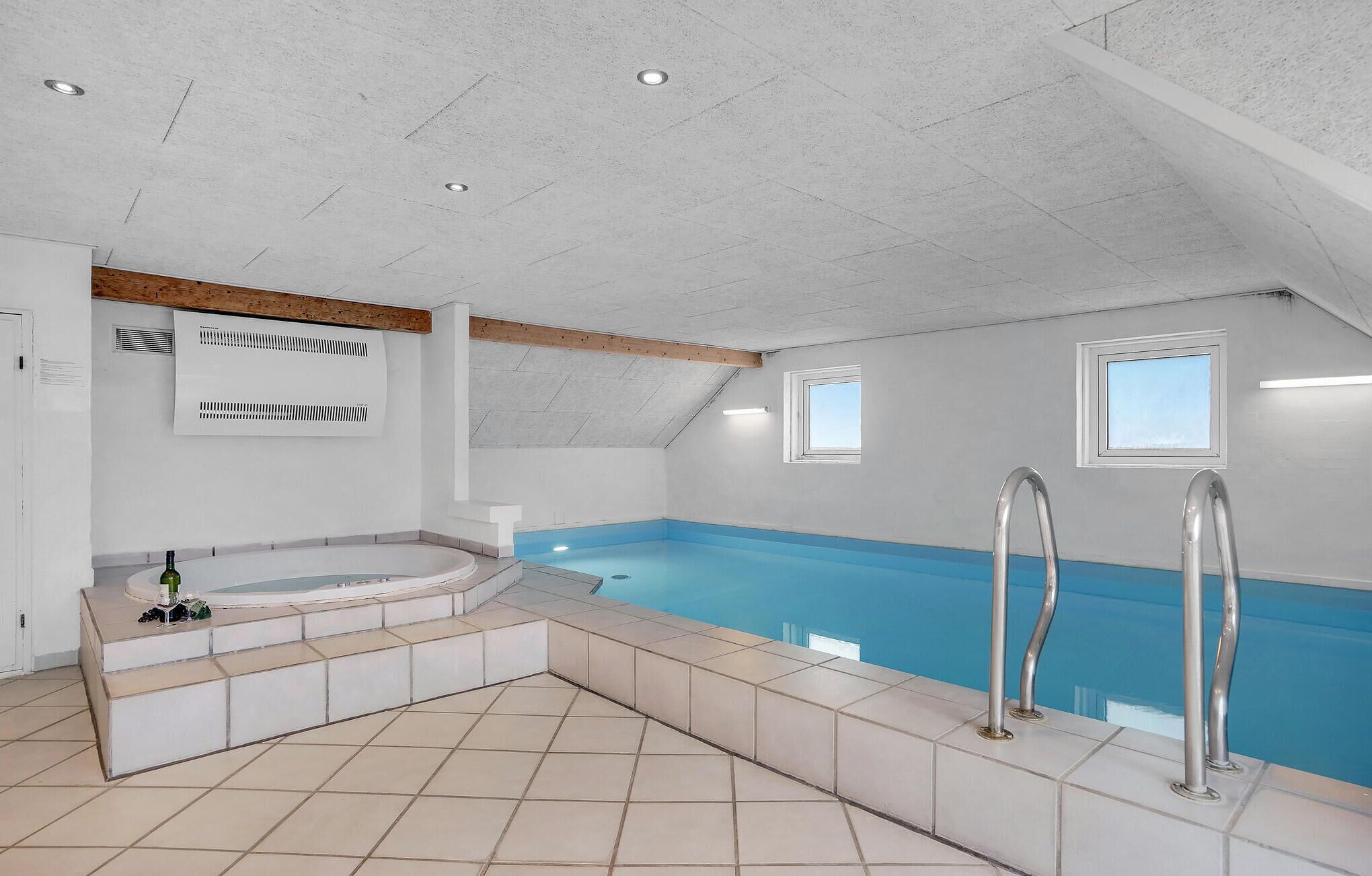 Ein moderner, überdachter Schwimmbereich mit Whirlpool, Fliesenboden und geneigter Decke.