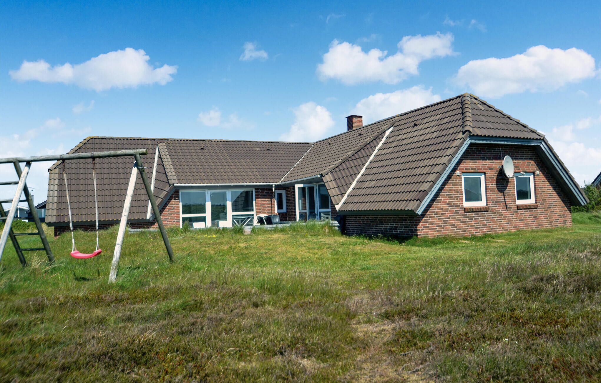 A two-story house with a sloped roof, a swing set, and a satellite dish.