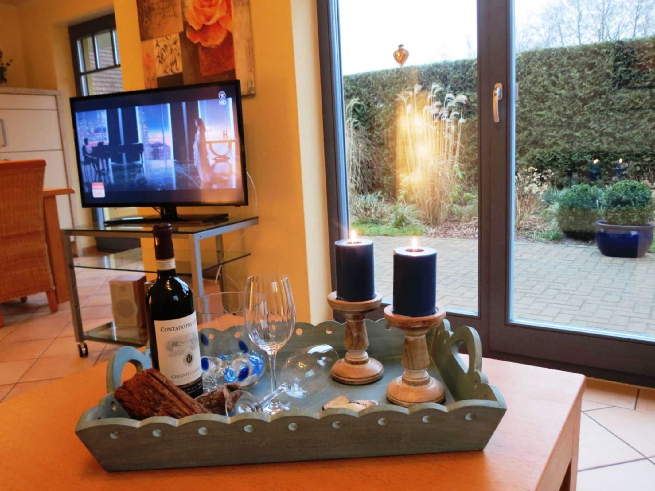 Quarto com televisão exibindo um filme, uma garrafa de vinho, copos e velas sobre uma bandeja.