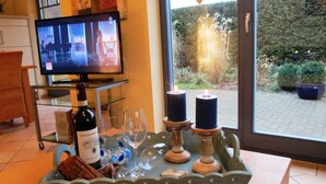 A room with a TV displaying a movie, a wine bottle, glasses, and candles on a tray. - Gray Heron Apartment (Prerow)