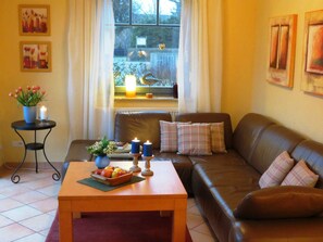 Ein gemütliches Wohnzimmer mit einer braunen Ledersofa, einem Couchtisch mit Früchten und einem kleinen Beistelltisch mit Kerzen und Blumen.