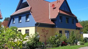 A two-story house with a red-tiled roof, blue and yellow exterior walls, and a white picket fence. - Gray Heron Apartment (Prerow)