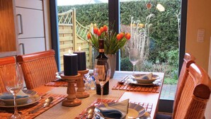 A dining table set with plates, cutlery, and candles, with a view of a garden through a glass door. - Gray Heron Apartment (Prerow)