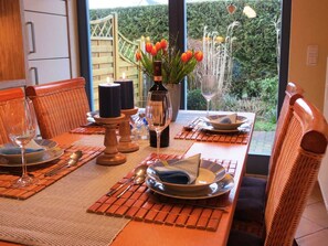 Mesa de jantar posta com pratos, talheres e velas, com vista para um jardim através de uma porta de vidro.