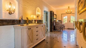 A spacious hallway with a marble floor, a light-colored wooden cabinet with drawers, a zebra-patterned chair, and a chandelier.