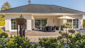 A two-story house with a tiled roof, a patio with outdoor furniture, and a large window.