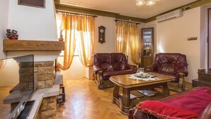 A living room with a fireplace, leather armchairs, a coffee table, and a red sofa. - 3 bedroom awesome home in Praputnjak (Praputnjak)