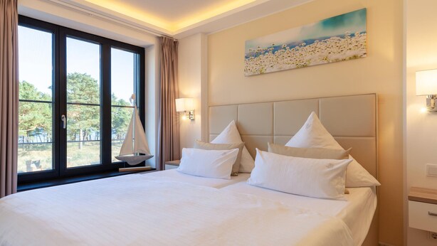 Habitación de hotel con una cama grande, un velero junto a la ventana y un cuadro en la pared.
