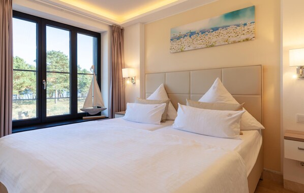 A hotel room with a large bed, a sailboat by the window, and a painting on the wall.