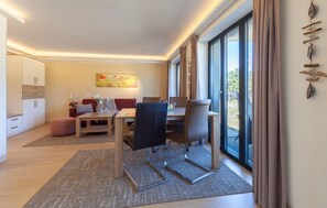 A modern hotel room with a dining area, a sofa, a coffee table, and a large window with curtains.