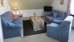 Un salon chaleureux avec deux canapés bleus, une table basse, un téléviseur et une petite table sur laquelle se trouvent une lampe et des fleurs.
