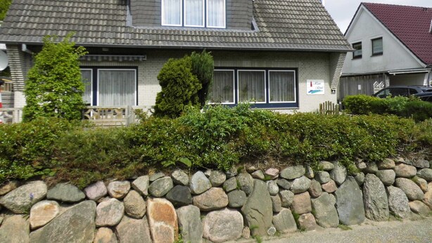 Une maison à deux étages, avec un mur de pierre à l’avant, un toit en tuiles et une enseigne sur laquelle on peut lire « Kaan Roni ».