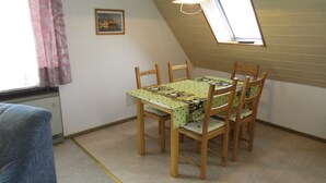 Une petite pièce agréable, avec un plafond en pente, une table à manger entourée de quatre chaises, une fenêtre unique ornée d’un rideau et un luminaire suspendu.