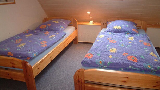 A small, cozy room with two wooden bunk beds, each with a purple floral bedspread.