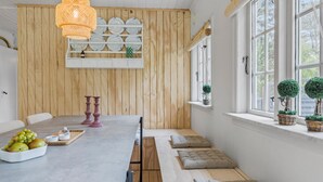 A dining area with a wooden wall, a long table, and a bench with cushions. - 3 bedroom beautiful home in Nexø (Nexø)