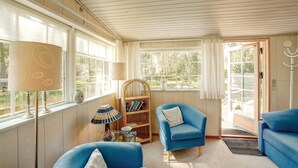A cozy living room with a blue sofa, a wicker chair, and a bookshelf. - 3 bedroom beautiful home in Nexø (Nexø)