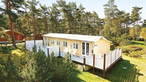 A small, single-story cabin with a fenced deck, surrounded by trees. - 3 bedroom beautiful home in Nexø (Nexø)