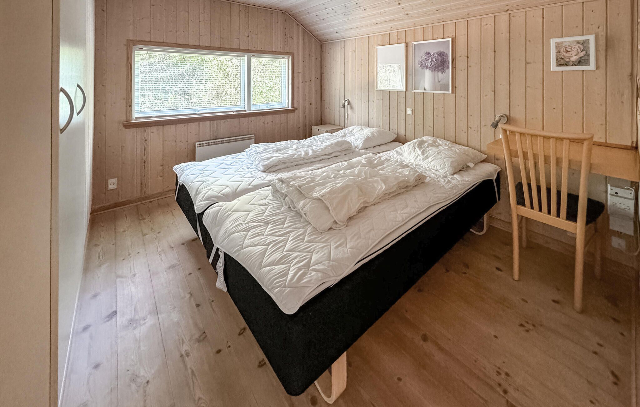 A bedroom with two beds, wooden walls, a window, and a chair.