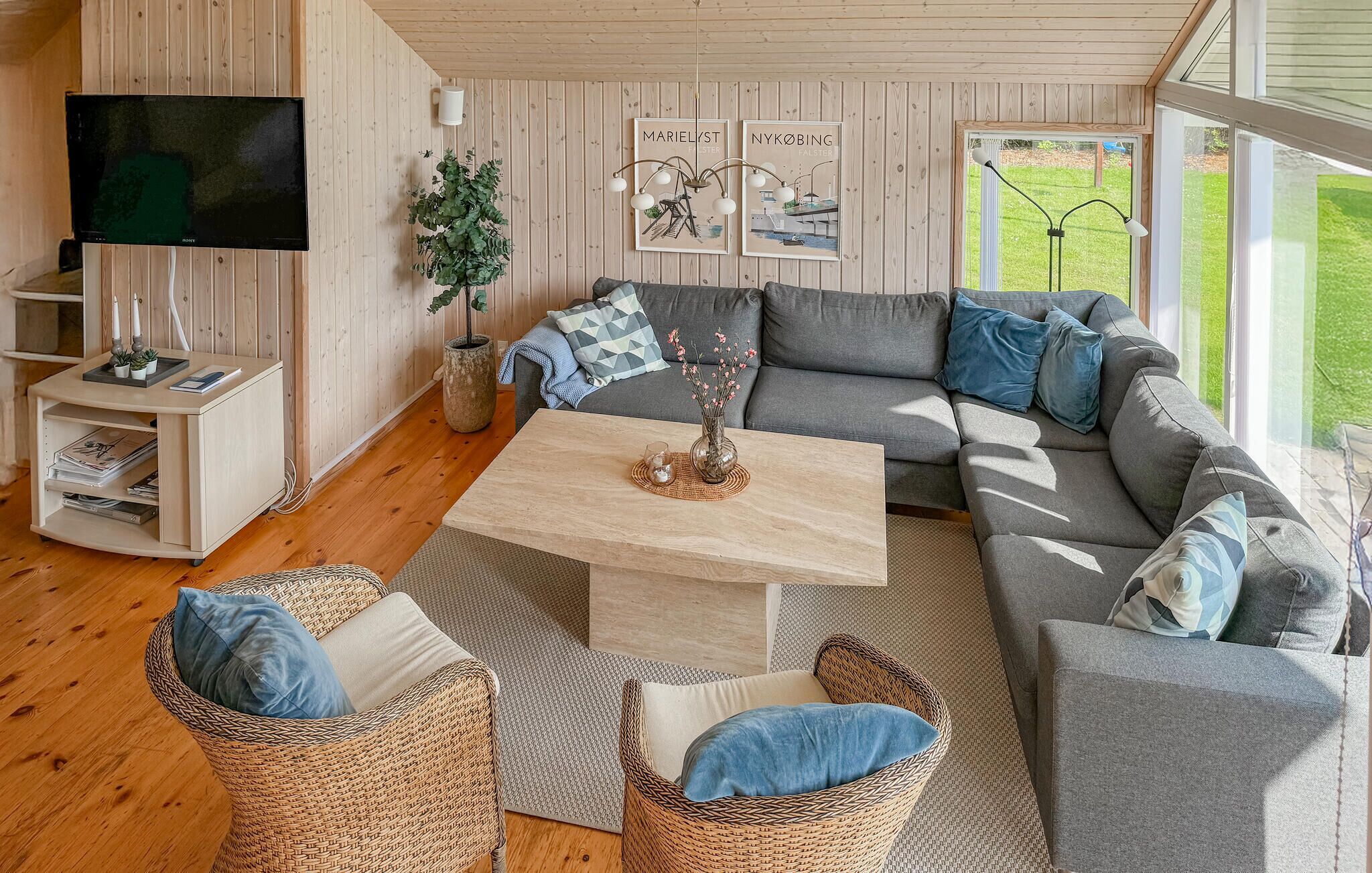 Un accogliente soggiorno con un divano grigio, poltrone in vimini, un tavolino in legno, una TV e quadri con immagini di uno skyline incorniciati alle pareti.
