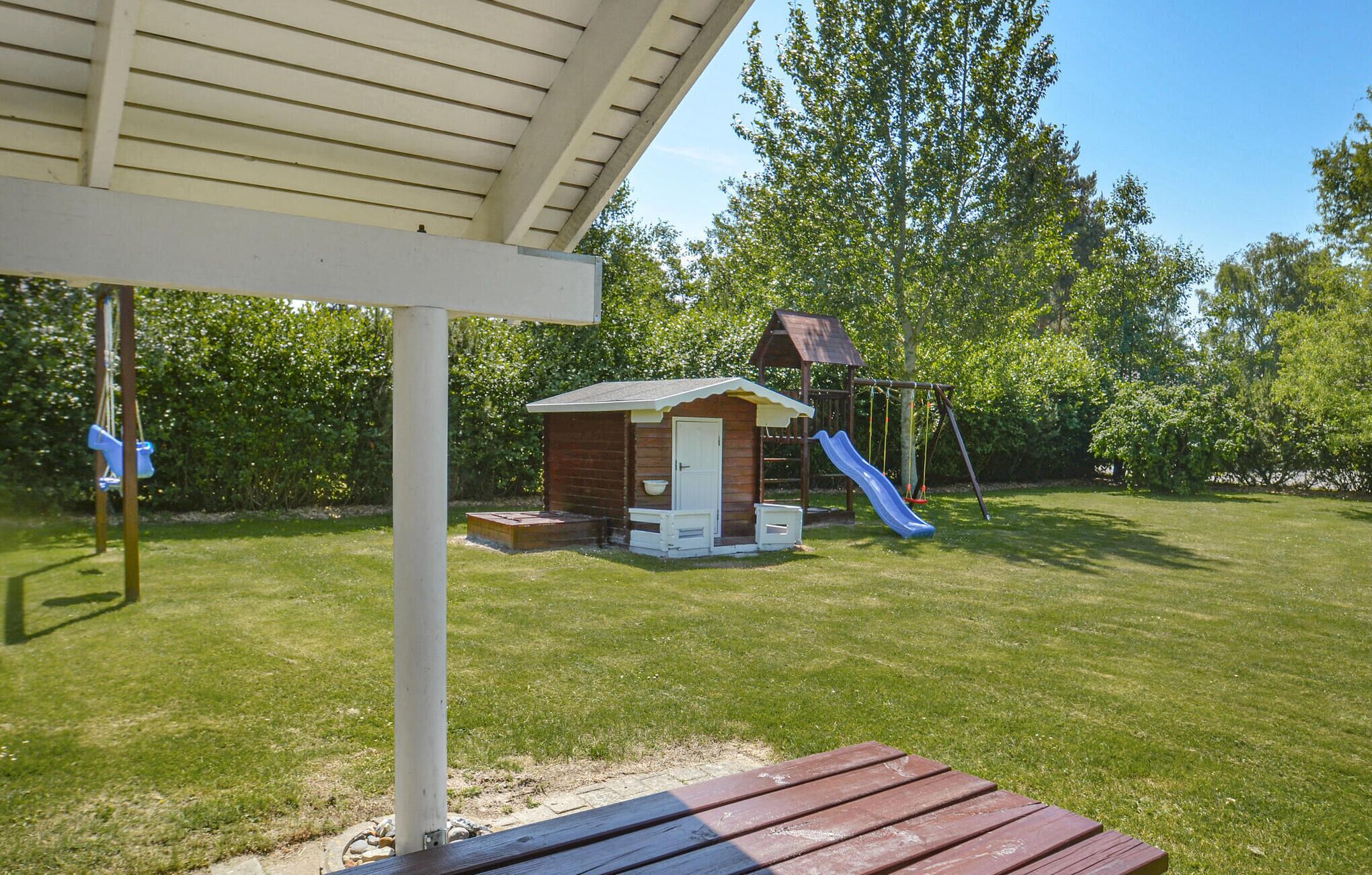 Un patio trasero con una casita de juegos de madera, un tobogán y un columpio.