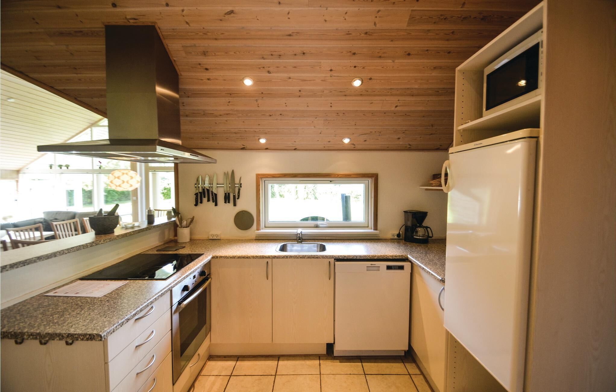 Eine kompakte Küche mit Herd, Backofen, Spüle und Geschirrspüler. Über der Spüle befindet sich ein Fenster und die Decke ist aus Holz.