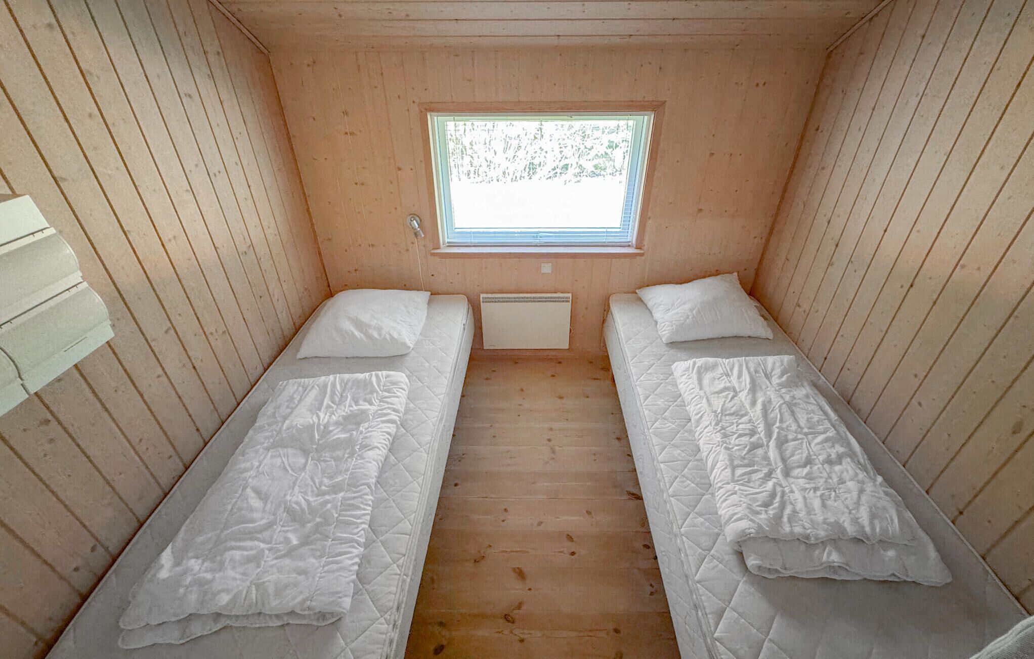 A small cabin with two single beds, a window, and wooden walls.