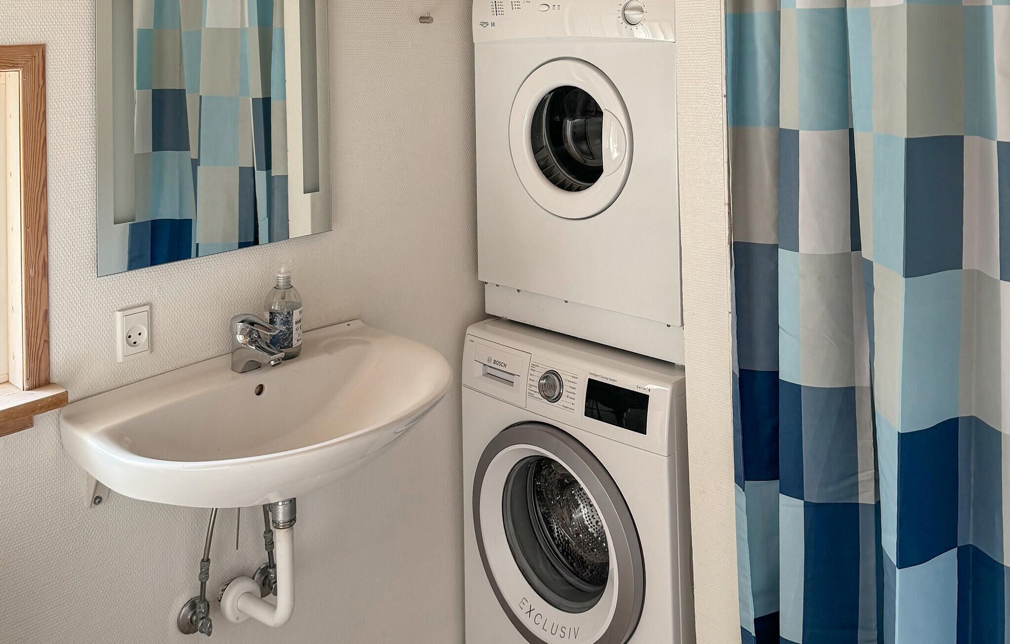 A compact bathroom with a sink, a Bosch washing machine, and a mirror.