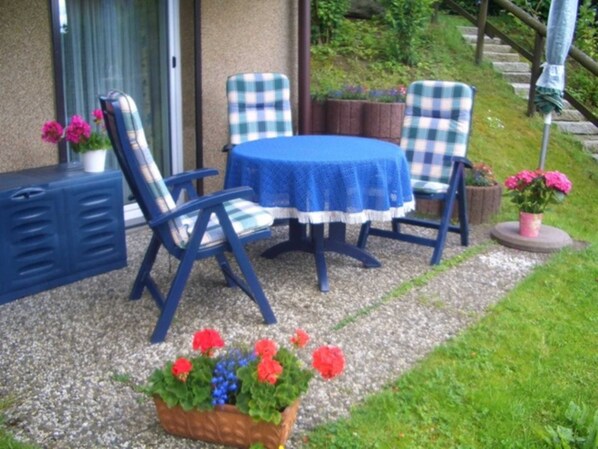 An outdoor patio with a table and chairs, a small garden area with flowers, and a staircase leading to a higher level.