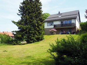 Une maison à deux étages avec un balcon, une pelouse et un grand arbre.