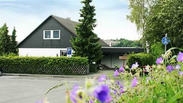 A house with a dark roof, white walls, a visible garage door, and a blue parking sign. - Vacation apartment Niewand (Clausthal-Zellerfeld)