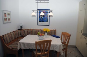 Un comedor con una mesa, sillas, un cuenco de fruta y un florero de flores.