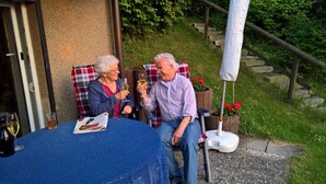 Two people seated at a round table with a blue tablecloth, a newspaper, and a bottle of wine. - Vacation apartment Niewand (Clausthal-Zellerfeld)