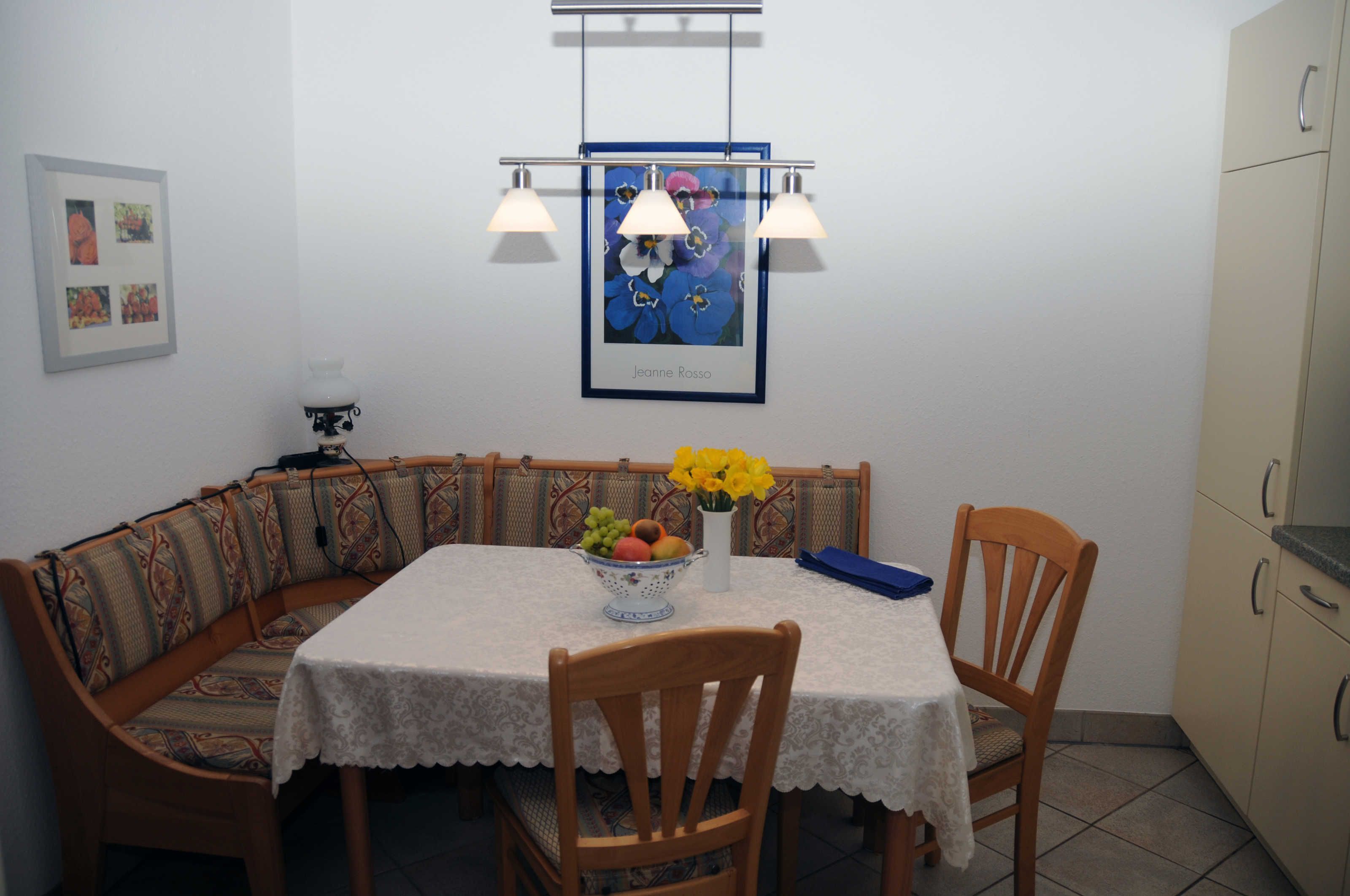 Een eethoek met een tafel, stoelen, een fruitschaal en een bloevas.