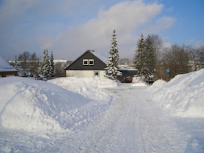 Un quartier résidentiel avec une maison, des arbres couverts de neige et une route.