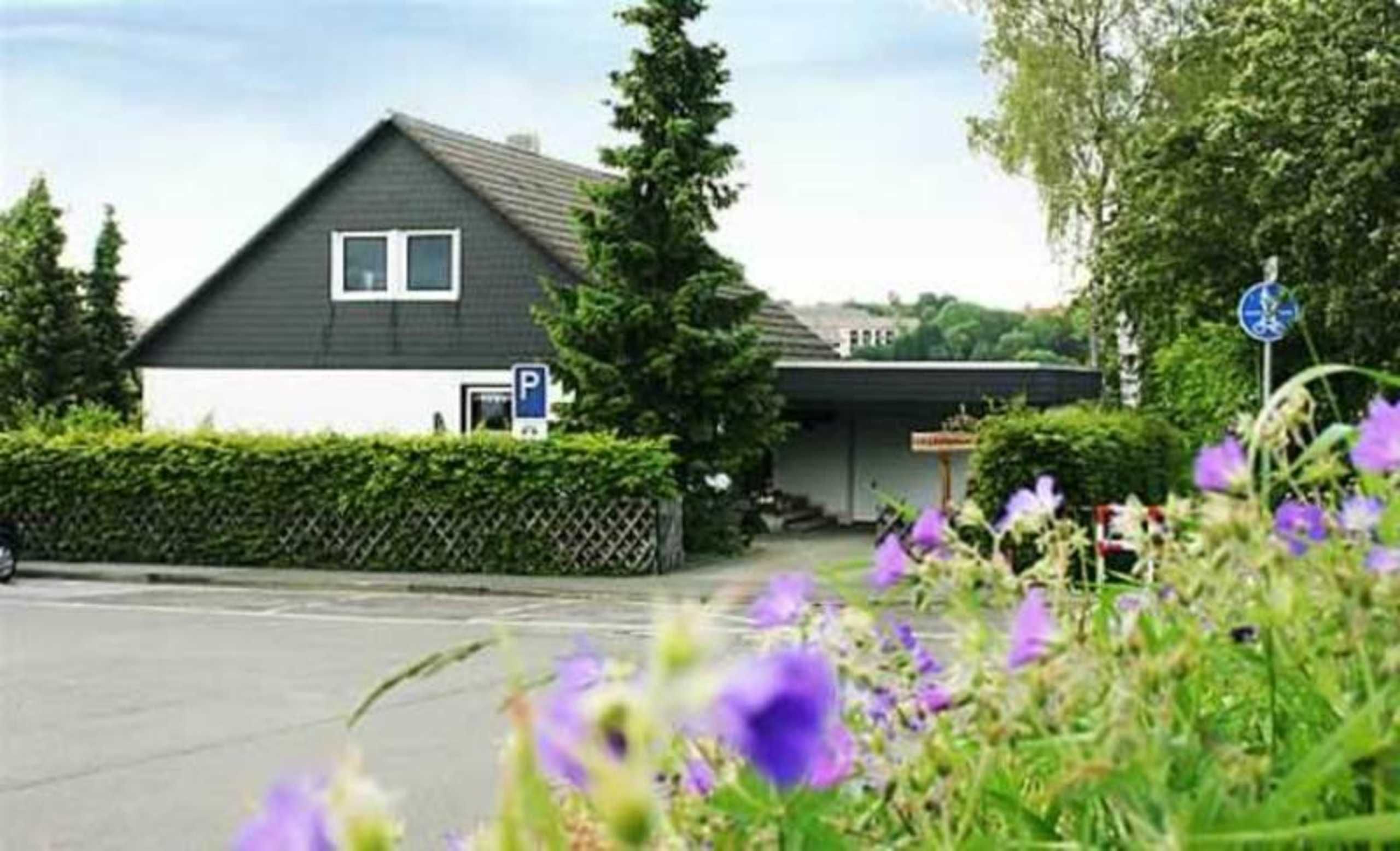Une maison avec un toit foncé, des murs blancs, une porte de garage visible et un panneau de signalisation bleu indiquant un espace de stationnement.