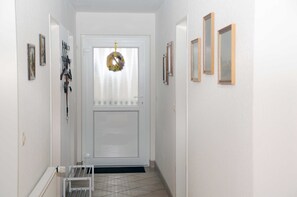 Un pasillo con una puerta blanca, una corona decorativa y cuadros en las paredes.
