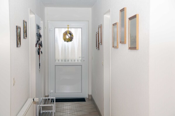 Un pasillo con una puerta blanca, una corona decorativa y cuadros en las paredes.