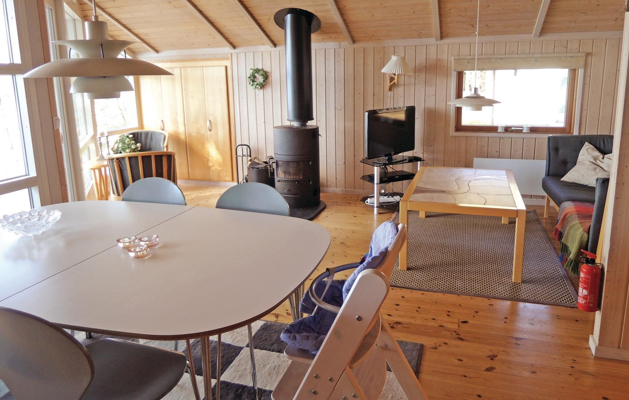Interior acogedor de una cabaña con una mesa de comedor, sillas, un sofá, un televisor y un estufa de leña.