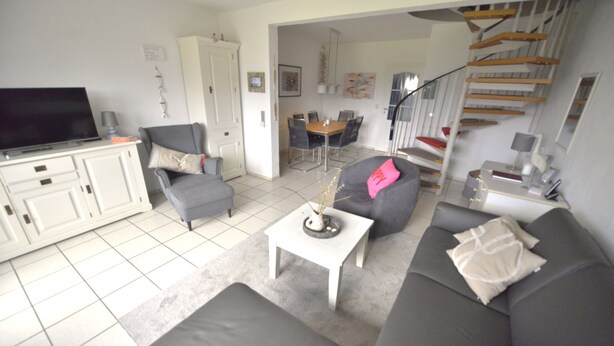 Un salon comprenant un canapé, un fauteuil, une table basse, un téléviseur et un escalier menant à une salle à manger.