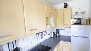 Une cuisine avec des meubles de couleur bois clair, un plan de travail noir, une cuisinière, un four à micro-ondes et un réfrigérateur.