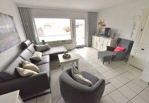Een woonkamer met een bank, fauteuil en een televisie op een kast.