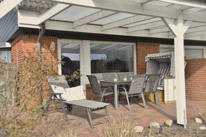 Een terras met een tafel en stoelen, een overdekt gedeelte en een bakstenen muur.