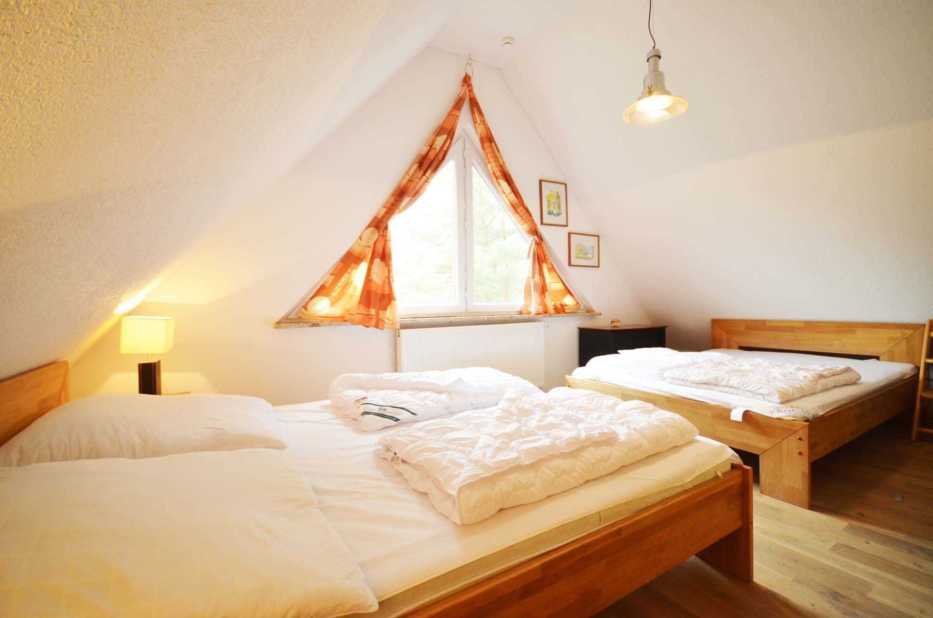 Une chambre avec deux lits, une fenêtre avec des rideaux, une lampe et une tête de lit en bois.