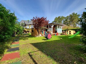 A residential backyard with a play area, including a slide and a tree with red leaves.