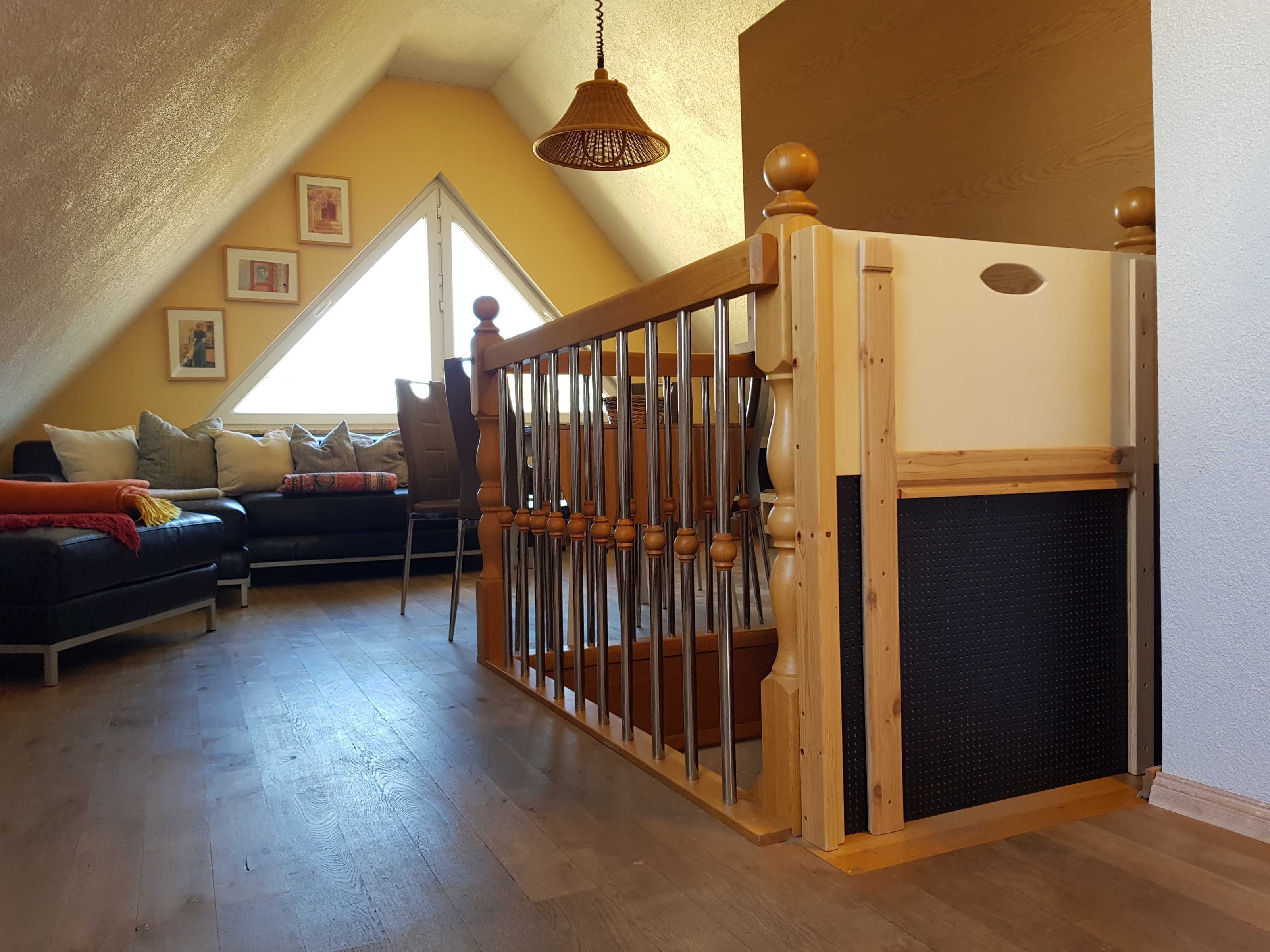 A cozy attic bedroom with a wooden staircase, a black sofa, and a large window.