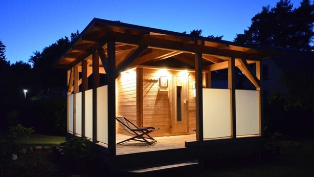A wooden cabin with a covered porch and a single lounge chair. - Apartment 3 - Vacation Home Strandstr. 29 (Loddin)