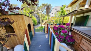 A wooden pathway leading to a building with a sloped roof, surrounded by colorful railings and a garden with purple flowers. - Apartment 3 - Vacation Home Strandstr. 29 (Loddin)
