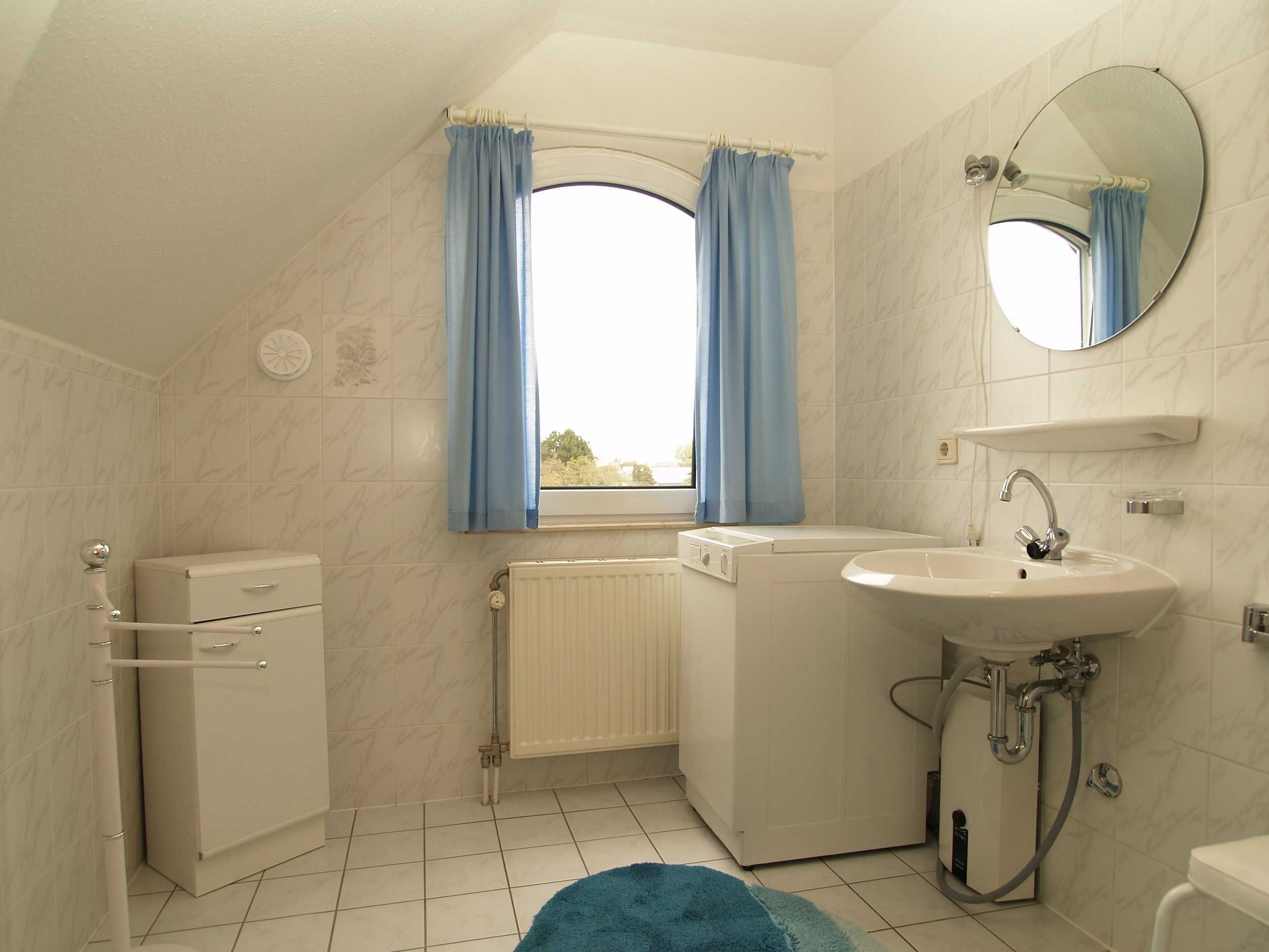 A small, modern bathroom with a window, a radiator, a washing machine, and a sink.