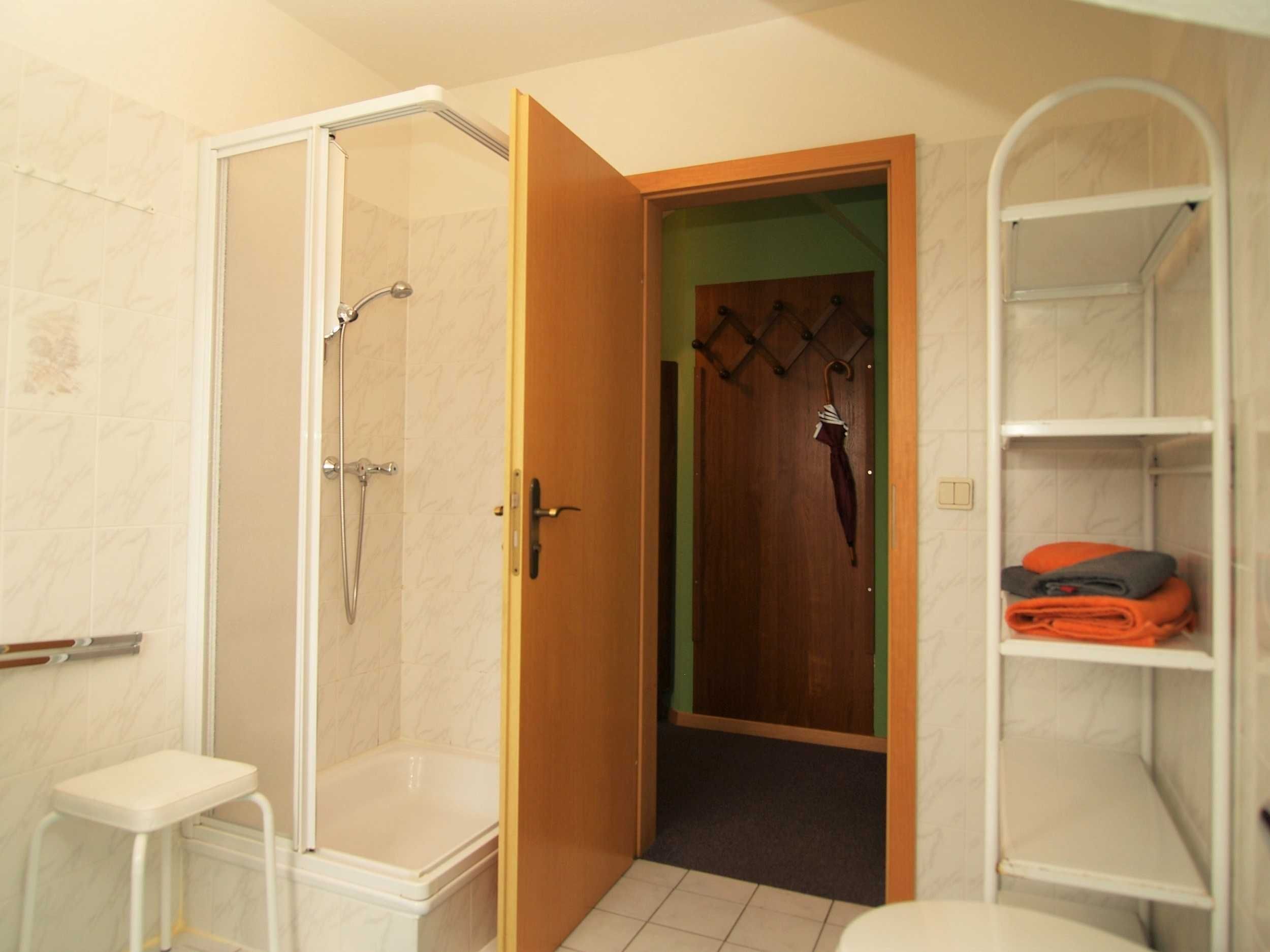 Ein Badezimmer mit Dusche, Toilette und einer Holztür, die zu einem Schrank mit Regalen führt.